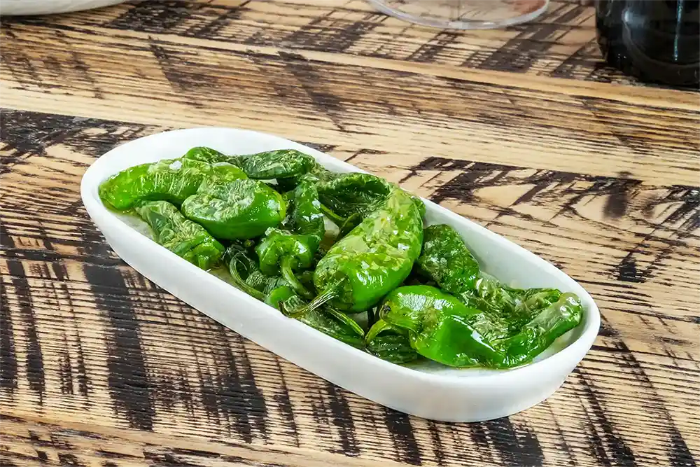 Discover a taste of Spain at our Tapas Restaurant in Manchester, where the classic Padrón peppers are served blistered and sprinkled with sea salt, offering a simple yet irresistible dish that promises a delightful gastronomic surprise with each bite. Perfect for sharing, these succulent green gems are a staple for any tapas lover and a must-try on our menu.